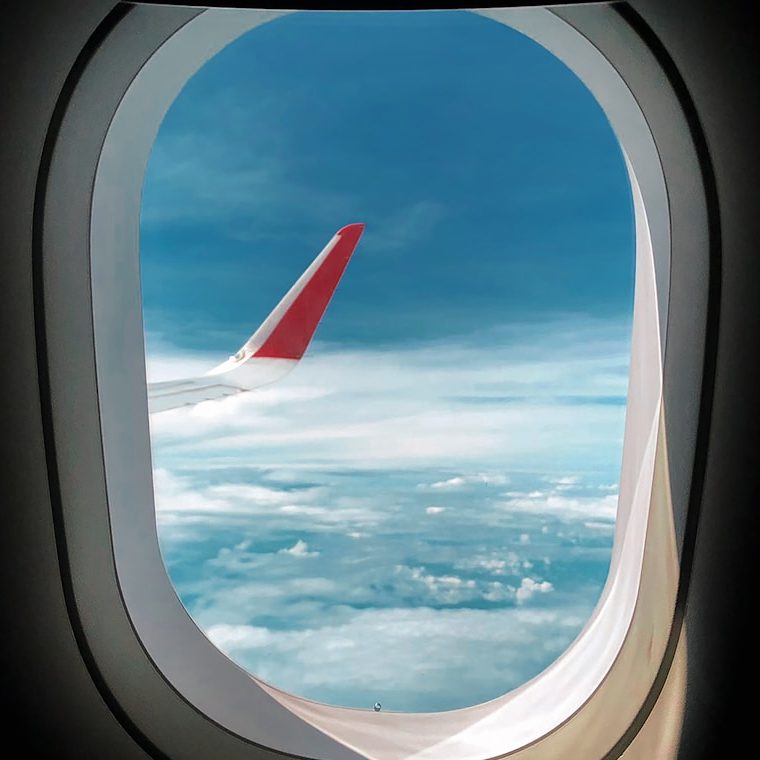 Vue depuis un hublot d'avion, montrant un aile et un ciel nuageux.