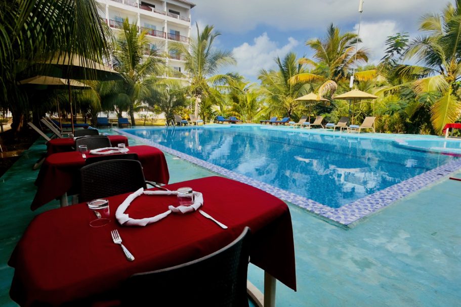 Table dressée avec couverts près de la piscine, entourée de palmiers et parasols.