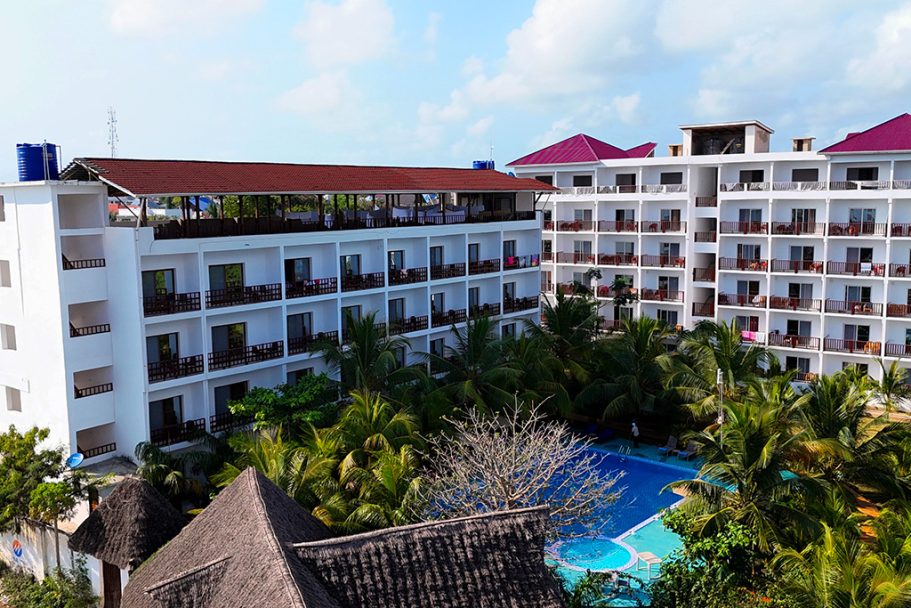 Complexe hôtelier avec piscine et jardins tropicaux, bâtiment blanc à plusieurs étages.