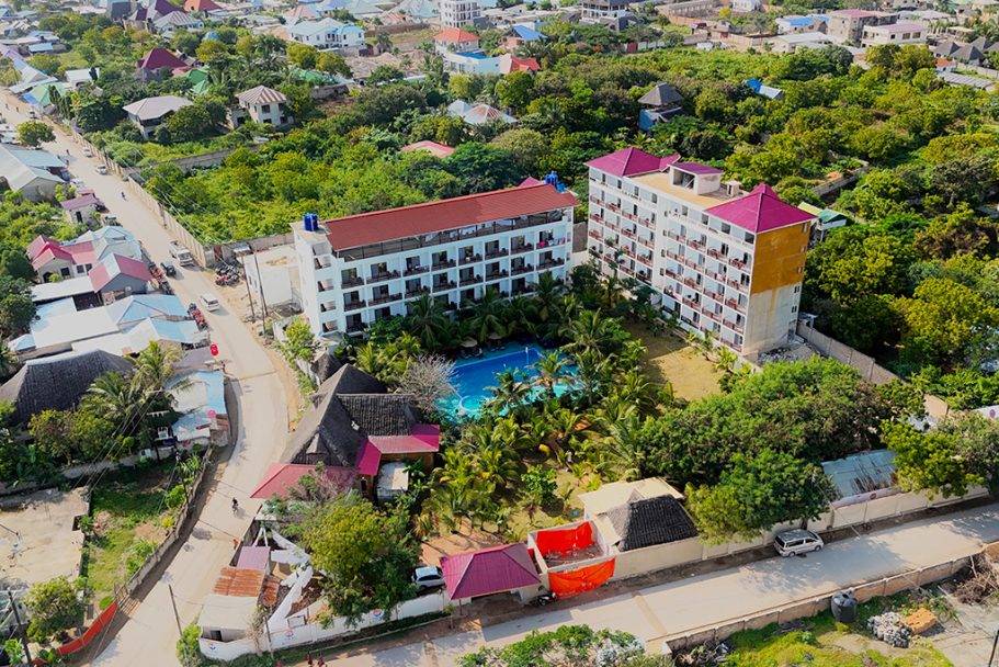 Vue aérienne d'un hôtel avec piscine entouré de verdure et routes adjacentes.