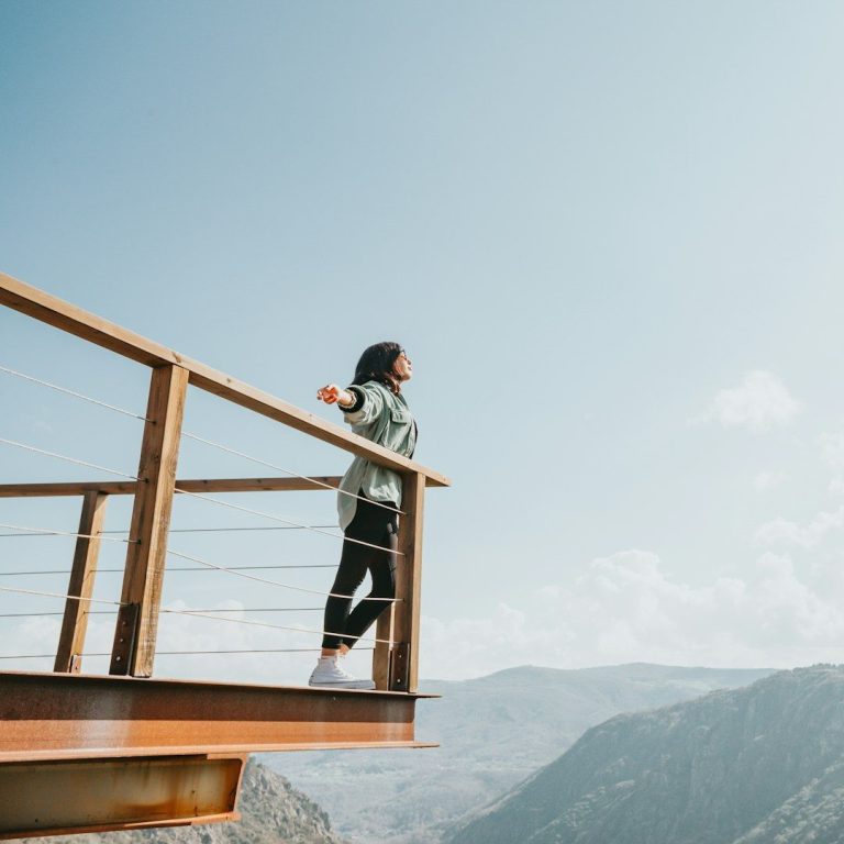 Femme contemplant un paysage montagneux depuis une terrasse en bois.