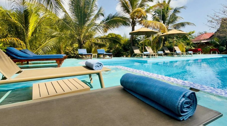 Chaises longues autour d'une piscine, entourées de palmiers et de verdure.