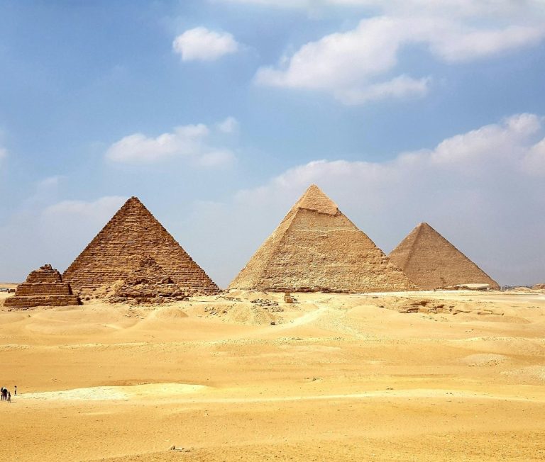 Trois grandes pyramides de Gizeh sur un paysage désertique sous un ciel bleu.