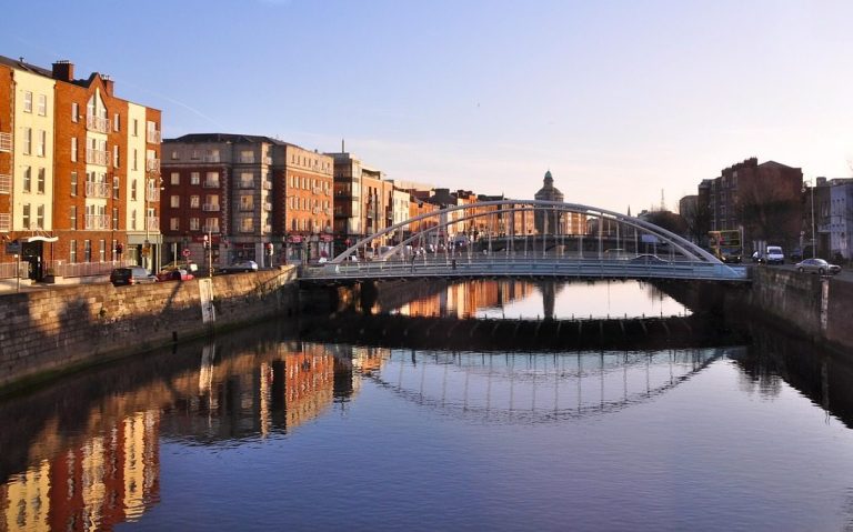 Pont en arc au-dessus d'une rivière, entouré de bâtiments colorés au coucher du soleil.