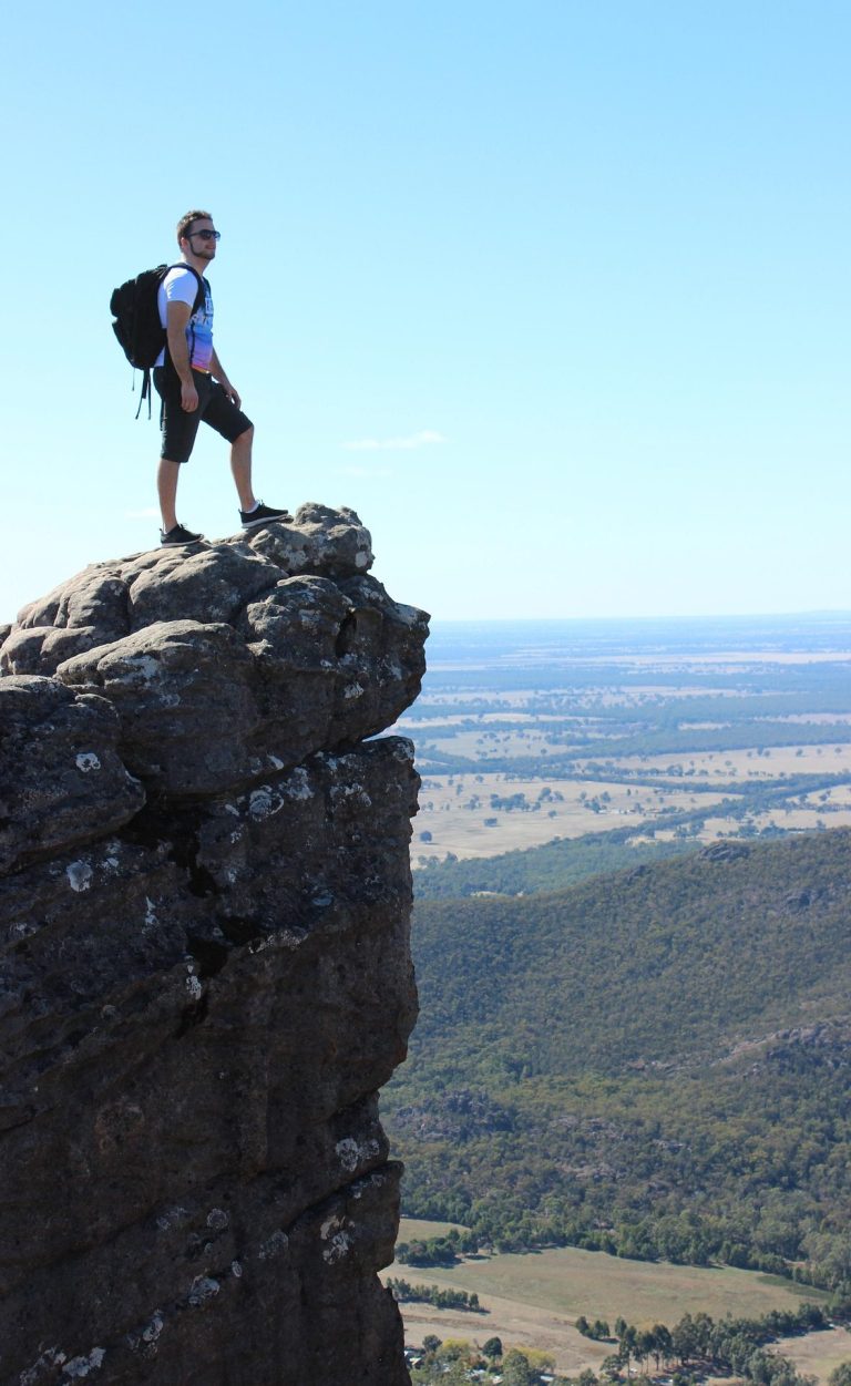 Homme debout sur un rocher au sommet d'une colline, vue panoramique sur la vallée.